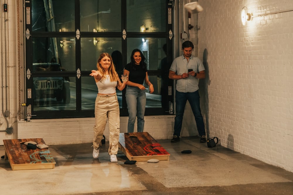 A woman throwing a beanbag while playing cornhole with friends at night