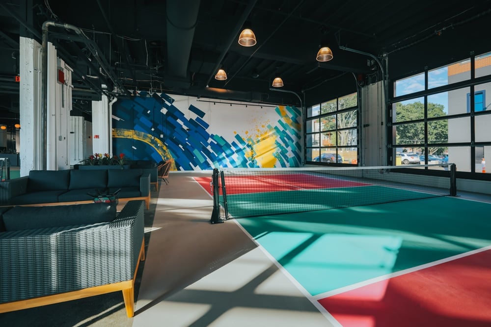 Indoor pickleball court with lounge seating and large glass windows.