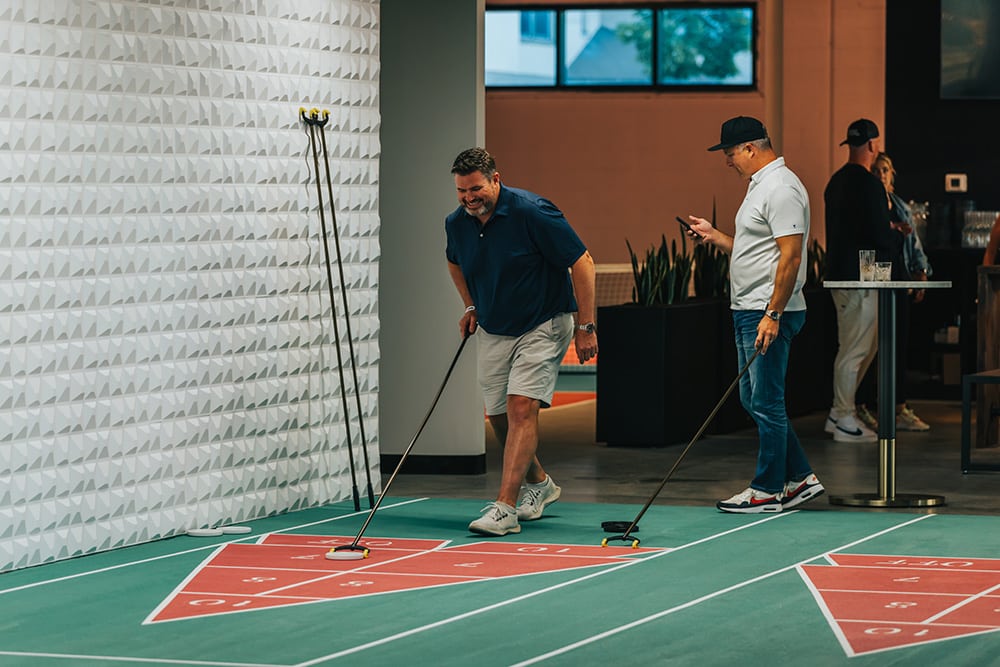 Two men playing shuffleboard indoors.