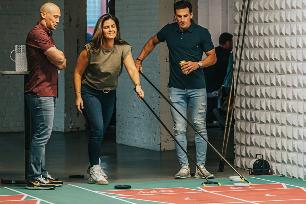 Three people playing shuffleboard on an indoor court