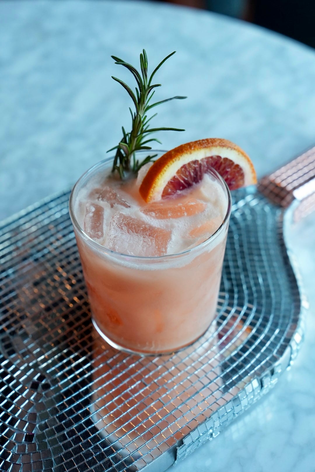 Close-up of a pink cocktail garnished with an orange slice and rosemary.
