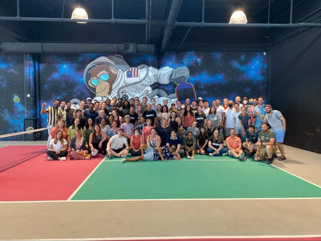 Large group of people posing together on an indoor pickleball court with a colorful space-themed mural in the background