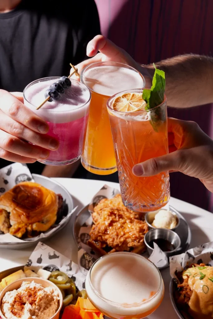 Friends toasting cocktails over a table of PKL’s signature bites and brunch dishes